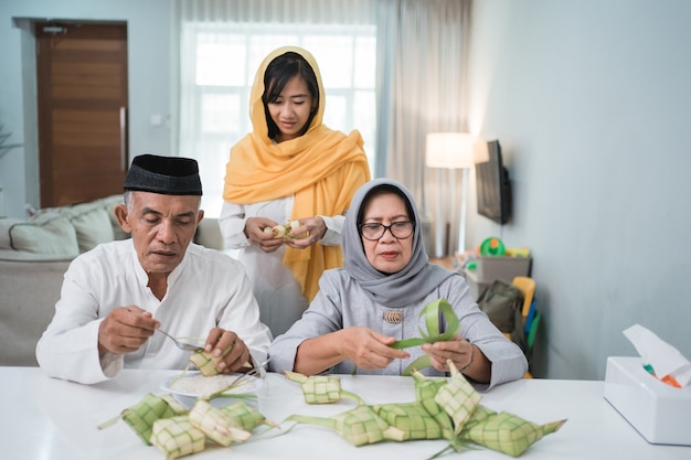 Senior moslimkoppel en dochter die ketupat maken voor eid fitr mubarak-viering thuis