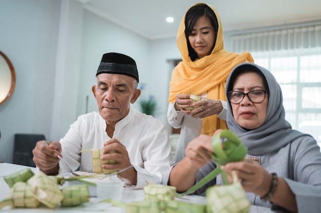 Senior moslimkoppel en dochter die ketupat maken voor eid fitr mubarak-viering thuis