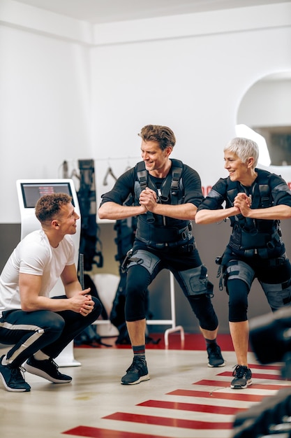 A senior mother and her middle age son have a EMS workout with personal trainer in the gym.