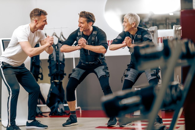 A senior mother and her middle age son have a EMS workout with personal trainer in the gym.