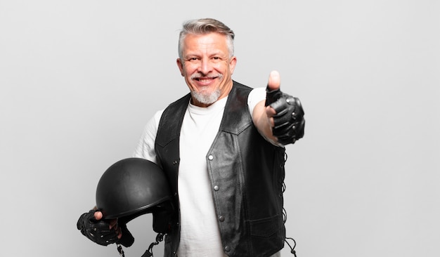 Старший мотоциклист чувствует себя гордым, беззаботным, уверенным и счастливым, позитивно улыбается и показывает палец вверх