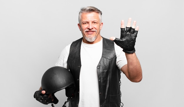 Senior motorbike rider smiling and looking friendly, showing number five or fifth with hand forward, counting down