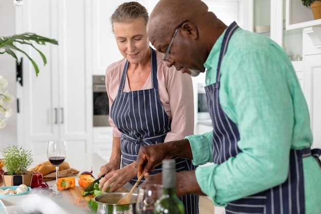 Senior multiracial couple in aprons preparing food together in kitchen at home. unaltered, lifestyle, retirement, togetherness, cooking, food, preparation.