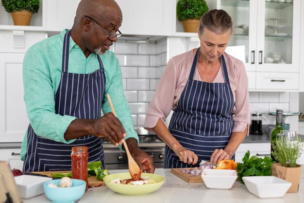 Senior multiracial couple preparing food together in kitchen at home. unaltered, lifestyle, retirement, togetherness, cooking, food, preparation.