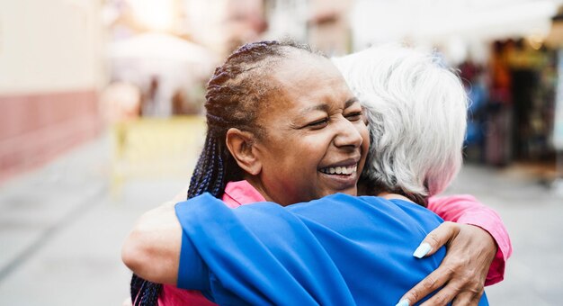 Photo senior multiracial women meeting and hugging each others outdoor focus on african female face