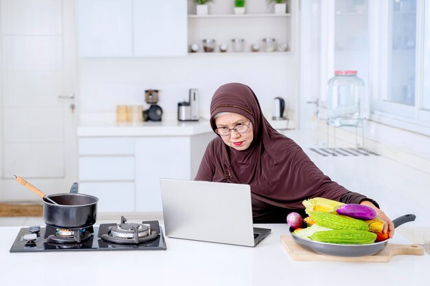 Senior muslim woman looking recipes at laptop