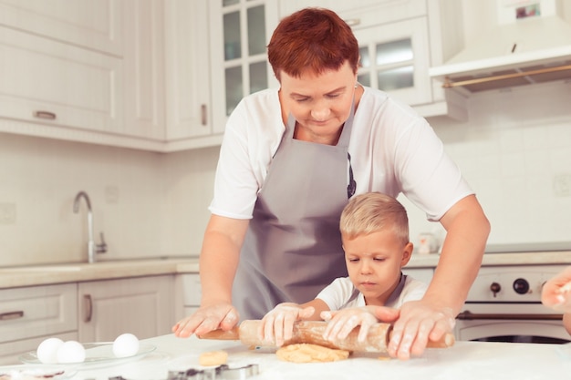 子供が生地を広げるのを手伝う先輩の乳母または祖母