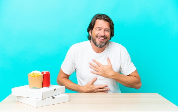 Senior Nederlandse man die fastfood eet, zittend in een tafel en veel lacht