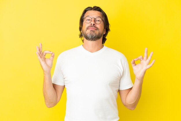 Senior Nederlandse man geïsoleerd op gele achtergrond in zen pose