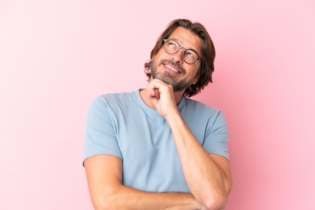 Senior Nederlandse man geïsoleerd op roze achtergrond met bril en denken tijdens het opzoeken