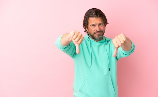 Foto senior nederlandse man geïsoleerd op roze achtergrond met duim omlaag met twee handen