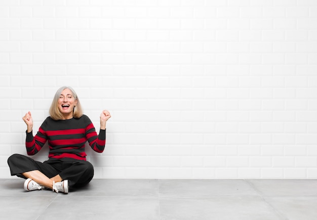 Senior of middelbare leeftijd mooie vrouw op zoek naar extreem blij en verrast, viert succes, schreeuwen en springen