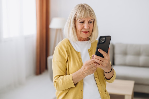 senior old elderly caucasian woman grandmother using smart phone in living room