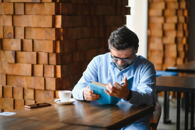 Senior old man reading a book in a coffee shop enjoying his literary hobby