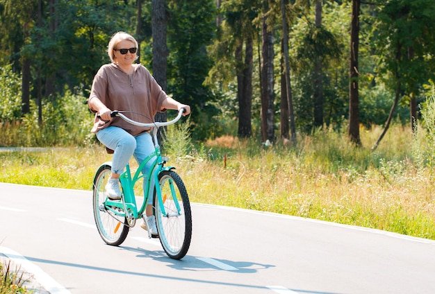 Senior older elderly modern woman rides a bicycle in a city park in the forest active pensioner heal