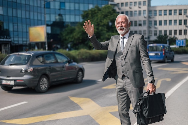 Senior ondernemer met laptoptas die op zonnige dag naar een taxi in de stad komt