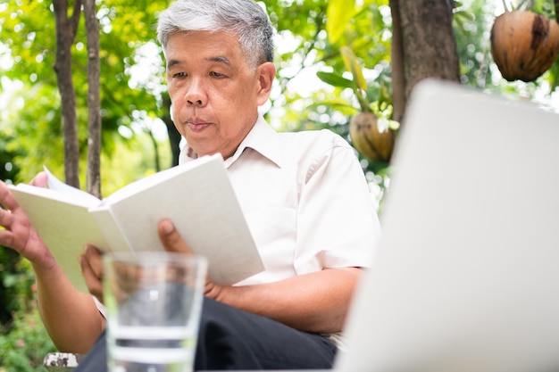 Senior oude man lezen van een boek in het park en drinkwater. Concept pensioen levensstijl en hobby.