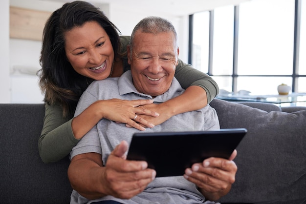 Senior paar gebruiken mobiele tablettechnologie video-oproep familie en communiceren met vrienden op de bank vanuit huis Gelukkige bejaarde grootouders ontspannen kijken naar grappige inhoud online en houden van het leven in pensionering