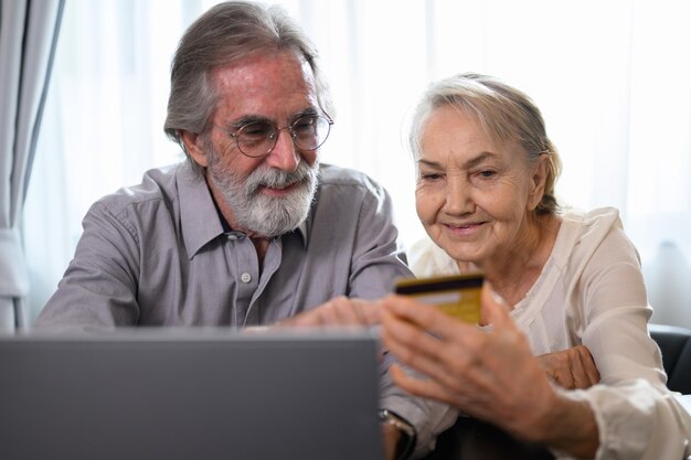 Senior paar gezonde grootvader en grootmoeder met behulp van laptop voor entertainment en winkelen