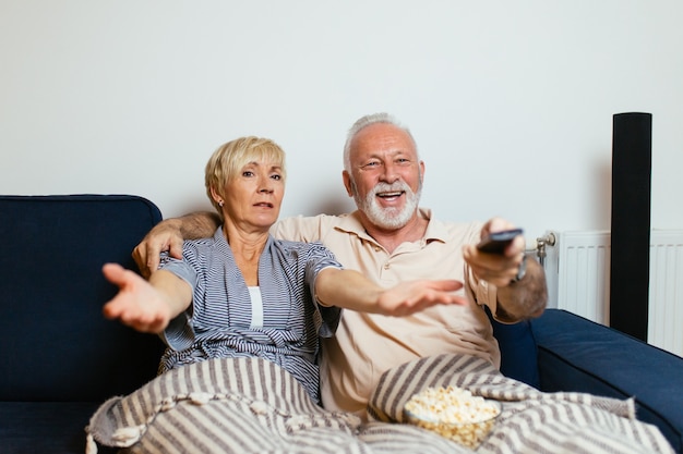 Senior paar liggend op bed en samen tv kijken.