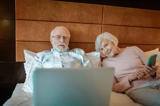 Senior paar liggend op bed in een hotelkamer en iets online kijken