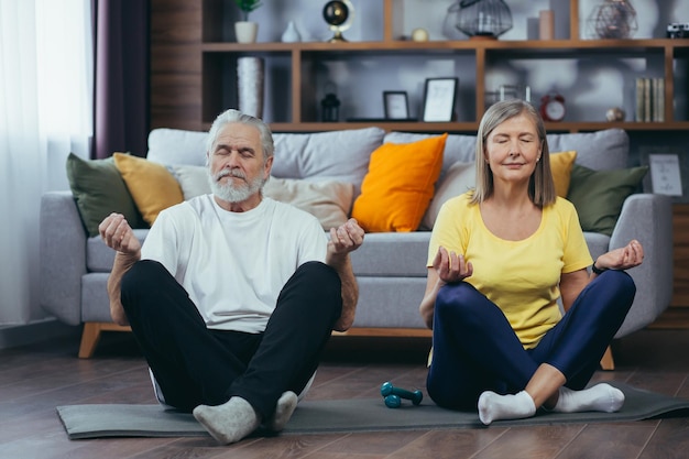 Senior paar man en vrouw samen thuis beoefenen van yoga mediteren zittend op de vloer in lotuspositie