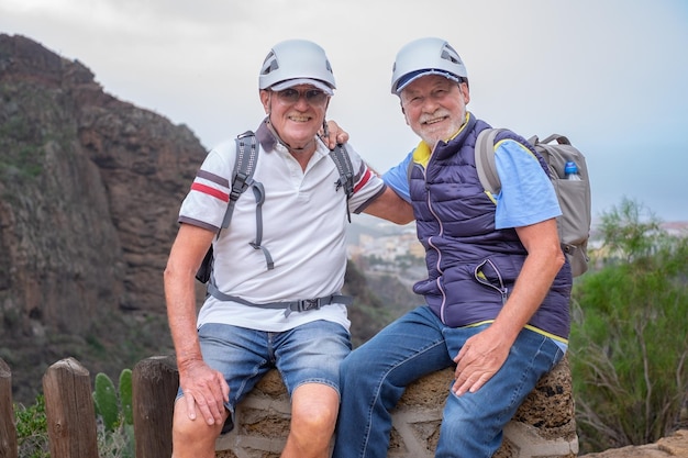 Senior paar mannen wandelaars met helmen en rugzakken rustend op de top van de berg glimlachend