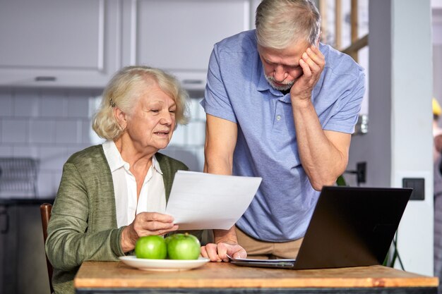 Senior paar rekeningen controleren tijdens het beheren van rekeningen op thuisbankieren app. casual grijsharige man en vrouw met behulp van laptop tijdens het kijken naar factuur en plan het budget om te besparen