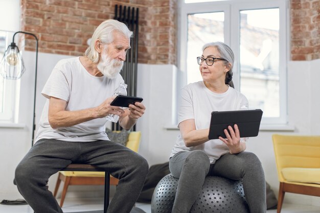 Senior paar rusten na de training met gadgets in handen