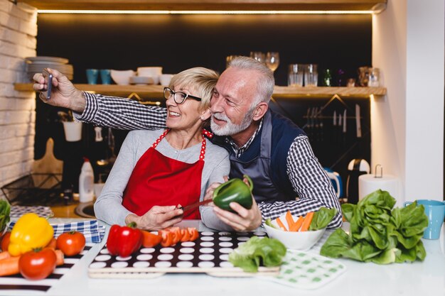 Senior paar selfie foto nemen tijdens het bereiden van lunch samen in de keuken.