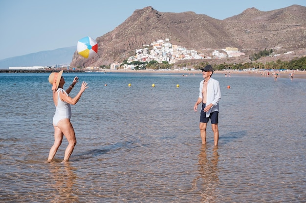 Senior paar spelen en plezier maken op het strand met de plastic bal Concept Lifestyle pensionering senior sporten