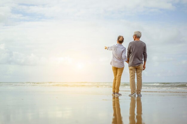 Senior paar staande op het strand hand in hand bij zonsopgang, plannen levensverzekering bij pensionering concept.