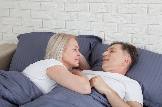 Senior paar thuis. De knappe oude man en de aantrekkelijke oude vrouw genieten van samen doorbrengend tijd terwijl liggend in bed. .