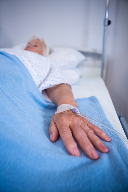 Senior patient hand with saline on bed in hospital