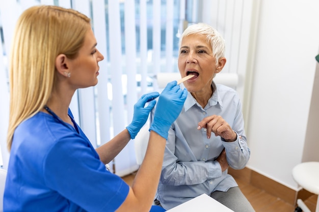 Senior patient opening her mouth for the doctor to look in her throat female doctor examining sore throat of patient in clinic otolaryngologist examines sore throat of patient
