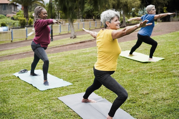 Senior people doing yoga class keeping social distance outdoor at city park