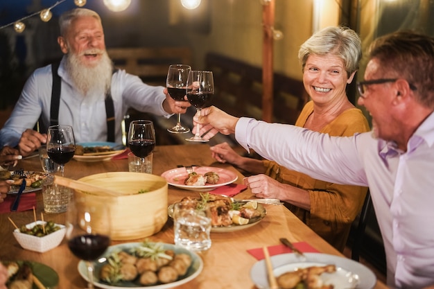 Senior people having fun cheering with wine at patio dinner - Focus on female face