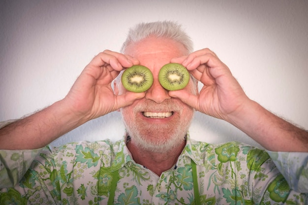 Senior people smiling holding two half kiwis in front of eyes old retired man in fun concept