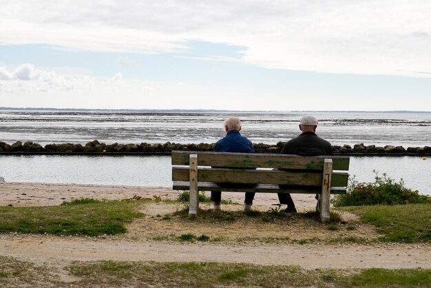 senior persoon gepensioneerd bejaarde echtpaar zittend op een houten bank kijkend naar de oceaan aan de Atlantische kust bij eb