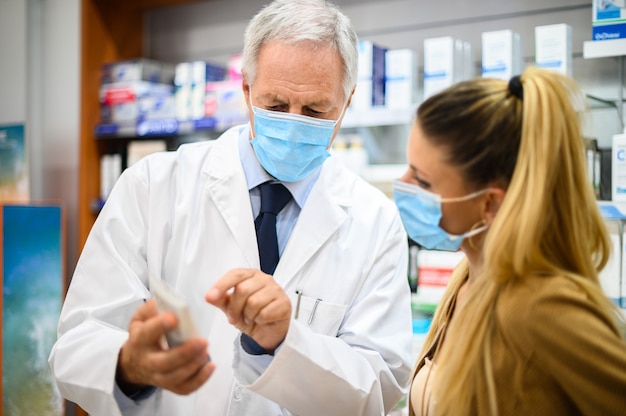 Senior pharmacist dealing with a customer, both of them wearing masks due to coronavirus