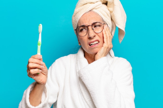 写真 バスローブを着て歯ブラシでシャワーを浴びた後の年配のきれいな女性