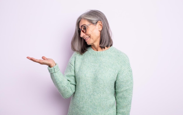 Senior pretty woman feeling happy and smiling casually, looking to an object or concept held on the hand on the side