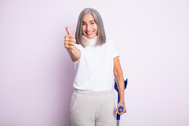 Senior pretty woman feeling proud,smiling positively with thumbs up. crutch and collar accident concept