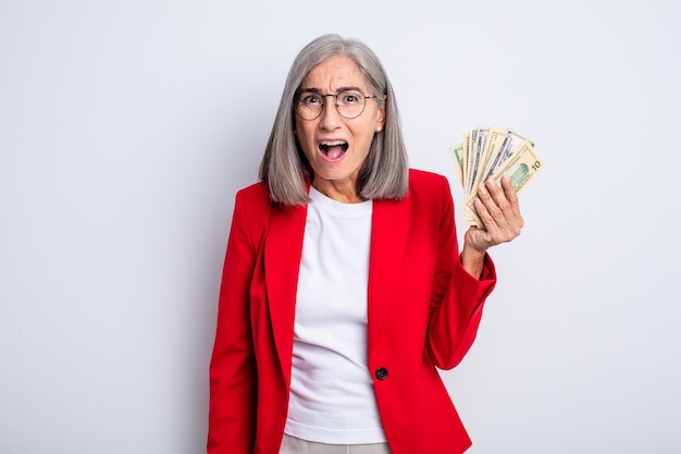 Senior pretty woman looking very shocked or surprised business and banknotes concept