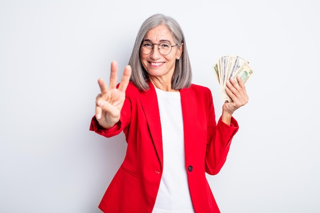 Senior pretty woman smiling and looking friendly, showing number three. business and banknotes concept