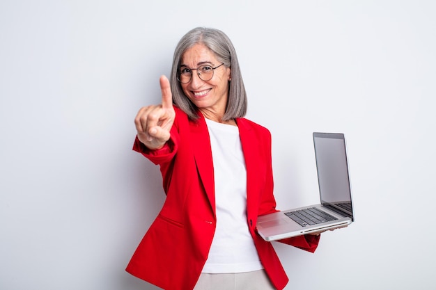 Senior pretty woman smiling proudly and confidently making number one. business and laptop concept