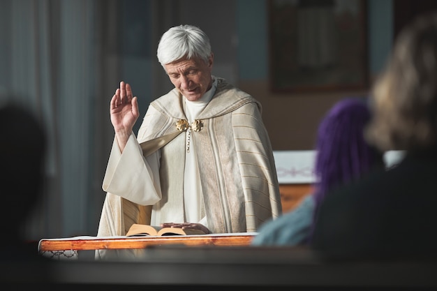 Sacerdote anziano che legge la bibbia per le persone durante la cerimonia in chiesa