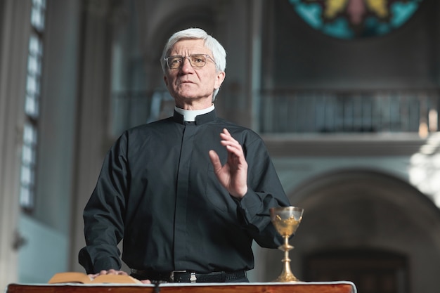 Senior priest standing at the altar and praying while serving in the church