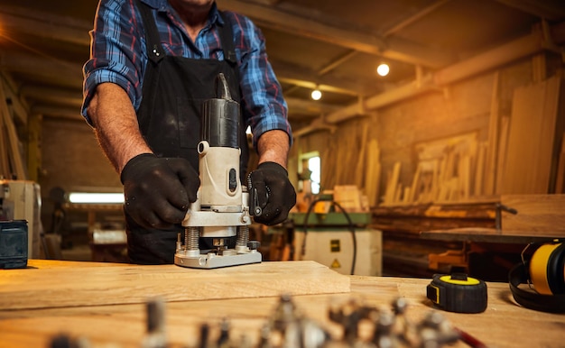 Senior Professional carpenter in uniform working of manual milling machine in the carpentry workshop