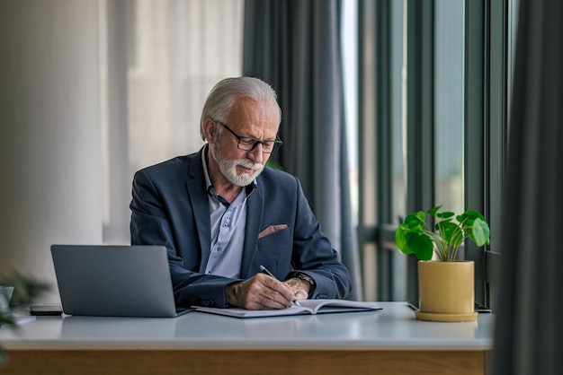 Senior professional making notes in diary while working at desk in office